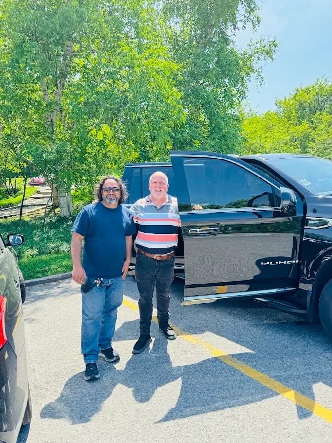 Two guests standing beside a black luxury SUV