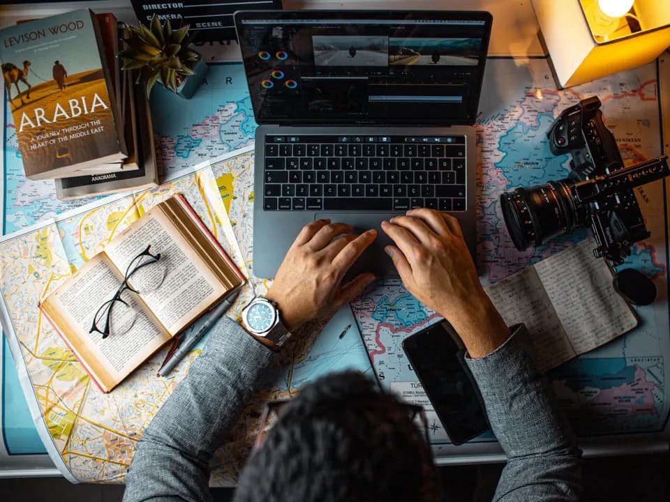 Travel planning workspace with a laptop, maps, notebook, and camera